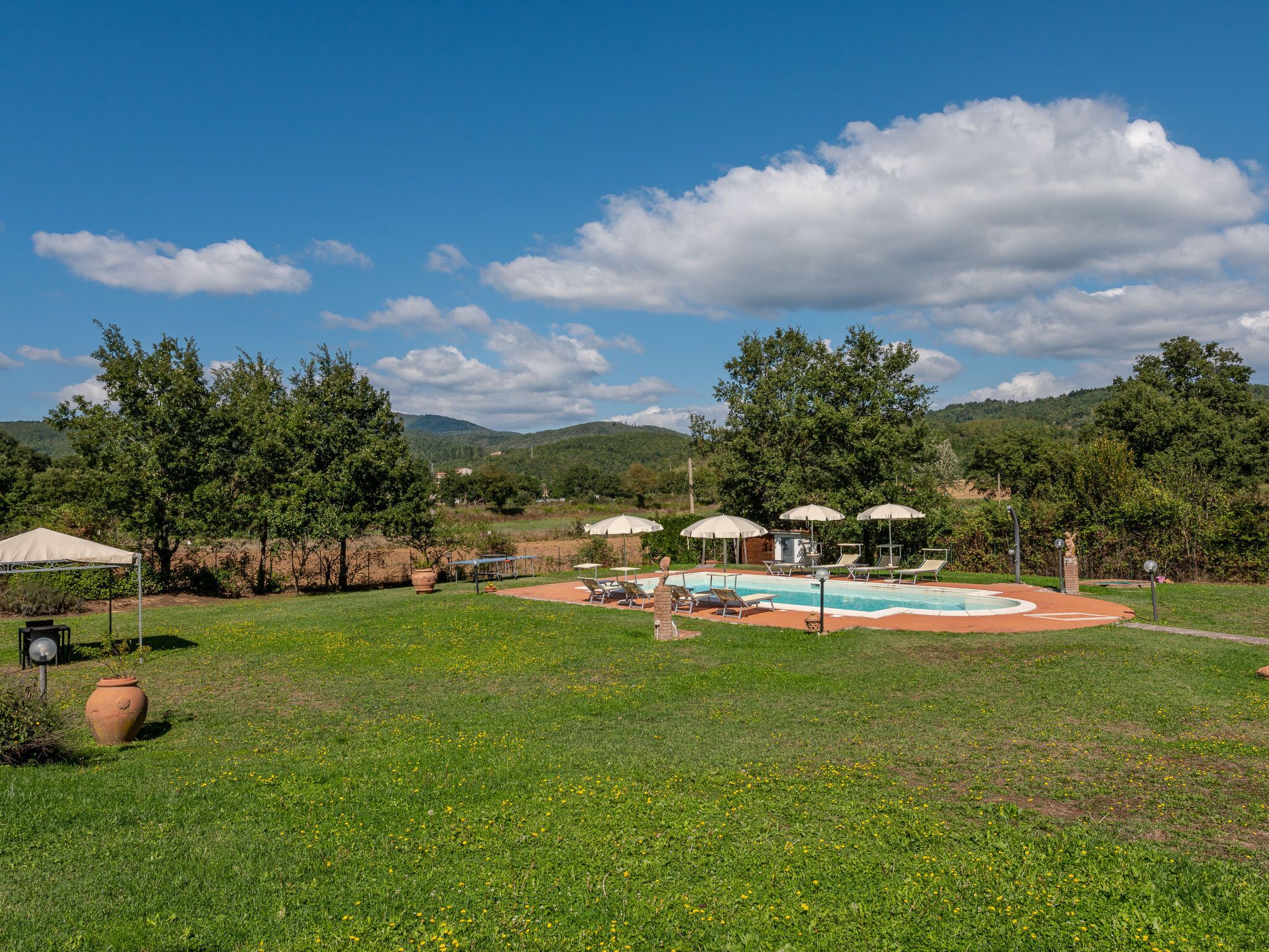 Un espace piscine agrémenté de chaises longues et de parasols, entouré de verdure et de collines.