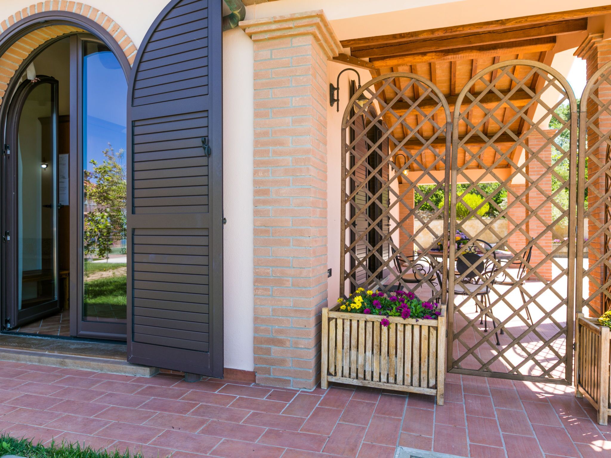 A patio area with a wooden lattice gate, a planter with flowers, and a brick wall.
