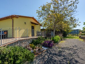 A yellow building with a stone wall and metal railing, surrounded by a garden with various plants and a gravel path. - Bellosguardo by Interhome (Roccastrada)