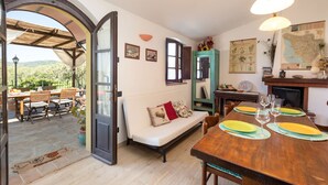 Ein gemütlicher Essbereich mit einem Holztisch, gedeckt für vier Personen, einer Couch und einem großen Fenster mit Blick auf einen Garten.