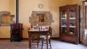 Una habitación acogedora con chimenea de piedra, una mesa de madera con sillas, un armario de madera con puertas de cristal y un reloj en la pared.