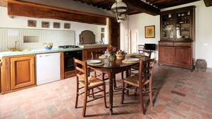Uma cozinha rústica com vigas de madeira, painel de azulejos e uma mesa de jantar posta para quatro pessoas.