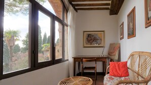Quarto com janelas amplas, teto de madeira, escrivaninha, cadeira e obras de arte nas paredes.