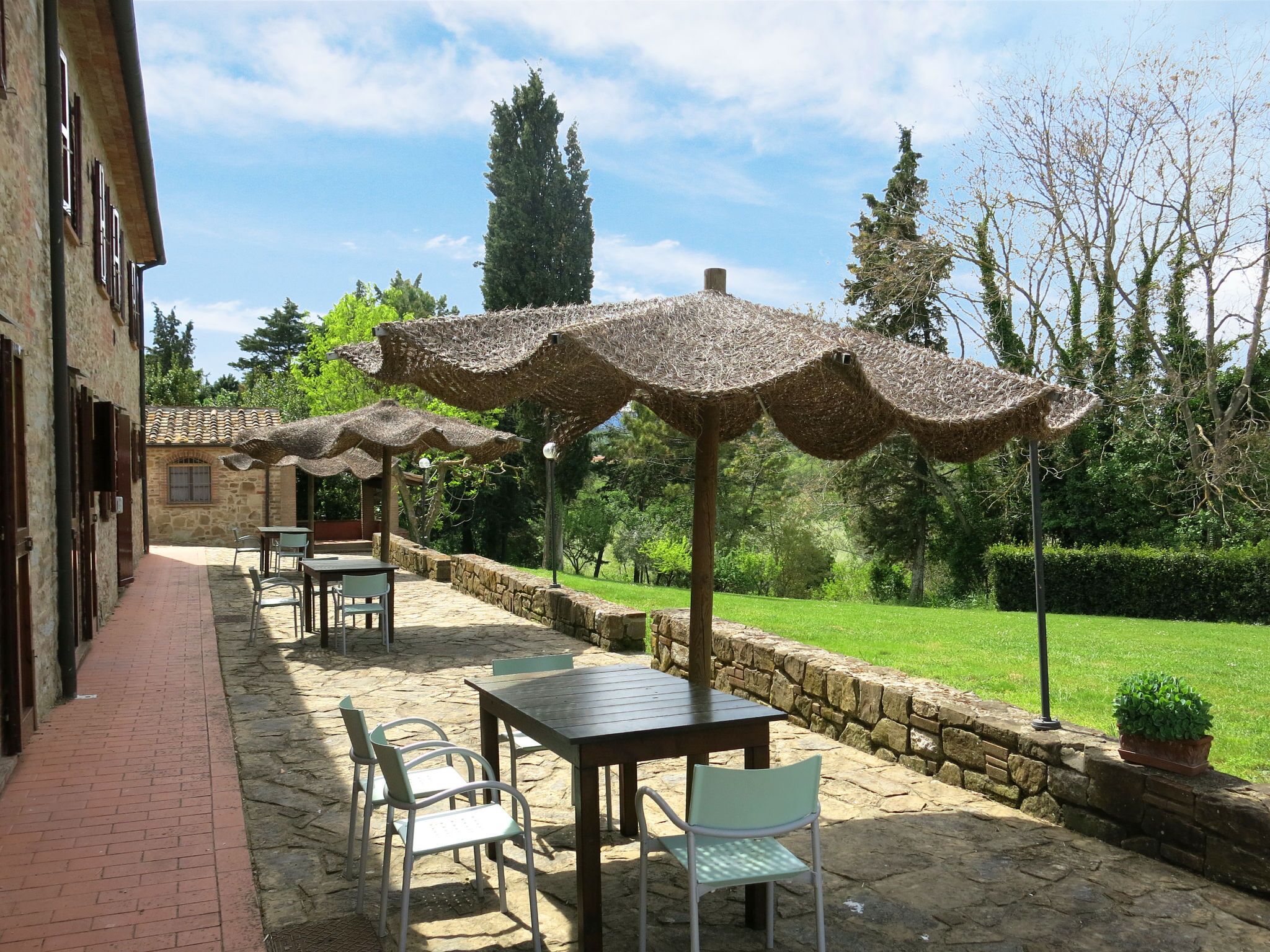 Une terrasse extérieure avec un sol en pierre, des tables, des chaises et des parasols en chaume.
