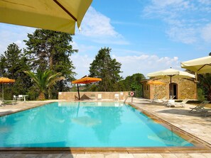 A swimming pool with lounge chairs and umbrellas, surrounded by trees and a stone building.