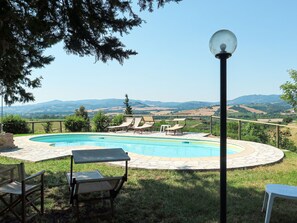 A swimming pool with lounge chairs and a lamp post, surrounded by a fence and greenery, with a view of distant hills. - Le Colmate by Interhome (Guardistallo)