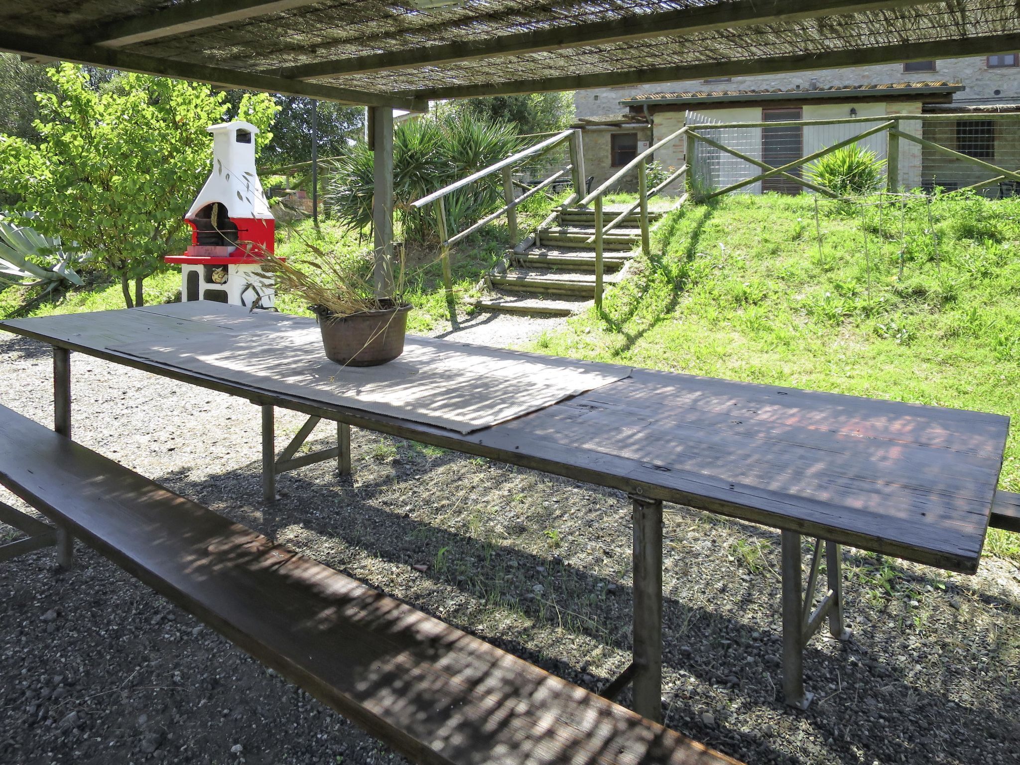 Ett picknickbord i trä med en bänk, en krukväxt och ett rött och vitt fågelhus.