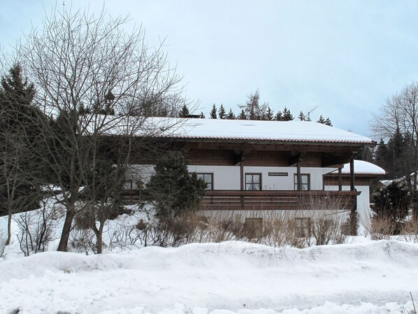 A two-story building with a snow-covered roof, surrounded by trees and a snow-covered ground.