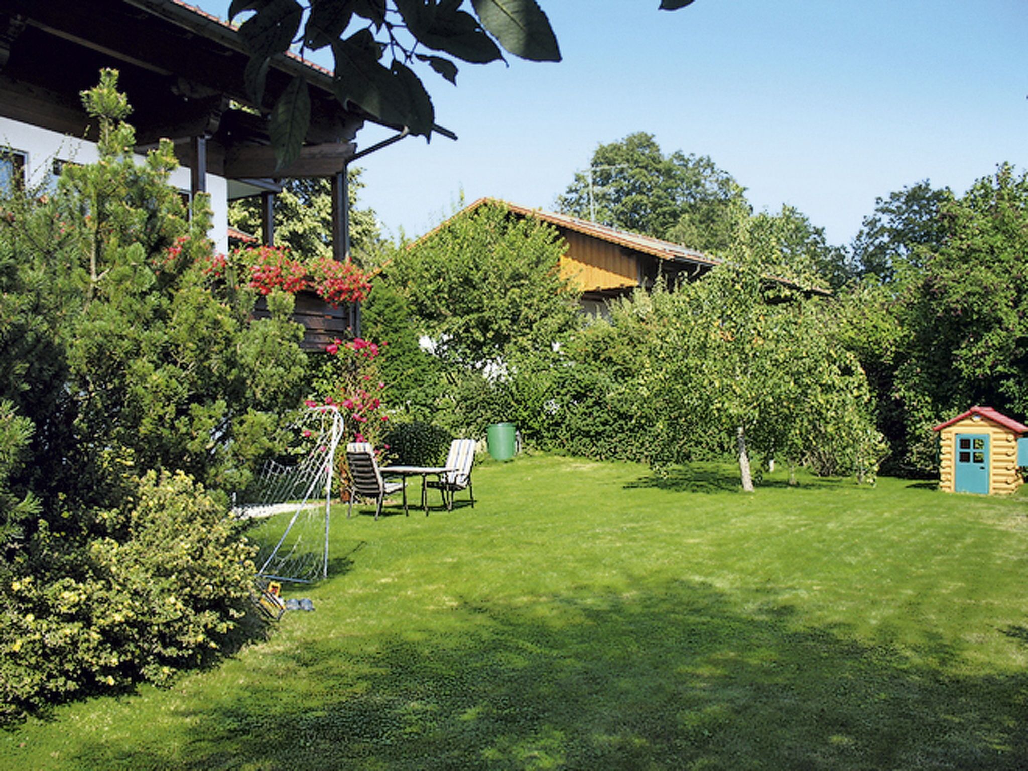 Un jardin bien entretenu, avec une pelouse, une petite maison de jeu en bois et un belvédère équipé de chaises.