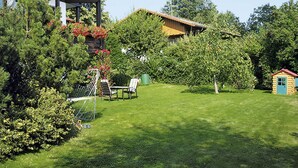 Un jardín bien cuidado con césped, una casita de juegos de madera y un mirador con sillas.