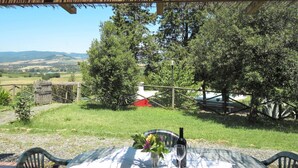 An outdoor patio with a table set for two, surrounded by chairs, overlooking a rural landscape with trees and a fence. - Le Colmate by Interhome (Guardistallo)