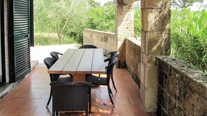 Une terrasse extérieure avec une table en bois et des chaises en osier, entourée de murs en pierre et de verdure.