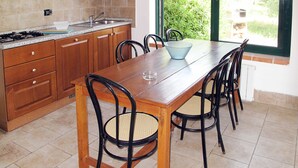 Une cuisine avec une table et des chaises en bois, une fenêtre donnant sur un paysage verdoyant et un mur recouvert de carreaux.