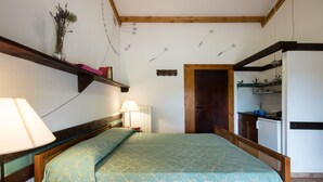 Un dormitorio con cama, mesita de noche, lámpara y cabecero de madera. Hay una estantería con libros y un jarrón de flores en la pared.
