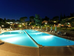 A large outdoor swimming pool with multiple lounge chairs and umbrellas, surrounded by trees and buildings.