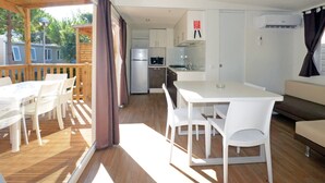 A modern kitchen with white cabinets, a built-in oven, and a sink. There is a dining area with a white table and chairs, and a wooden deck outside. - Campeggio del Forte by Interhome (Marina di Bibbona)