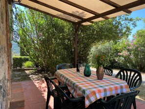 An outdoor patio with a checkered tablecloth, chairs, and a vase of flowers.