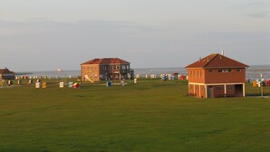 A coastal area with two brick buildings, a grassy field, and a body of water in the background. - Apartment Harms by Interhome (Horumersiel)