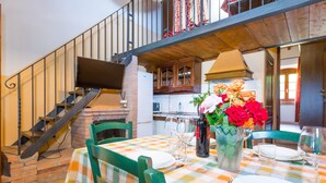 A dining area with a checkered tablecloth, green chairs, a vase of flowers, and a brick fireplace. - Apartment Lepre by Interhome (Riparbella)