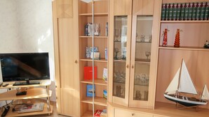 Un salon doté d’un téléviseur à écran plat, d’étagères en bois remplies de livres et d’objets décoratifs, ainsi que d’une maquette de petit voilier.