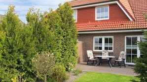 Une maison à deux étages avec un toit recouvert de tuiles rouges, une façade en briques et une petite terrasse avec une table et des chaises.