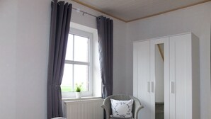 Une chambre avec deux lits, une armoire, une chaise et une fenêtre avec des rideaux.