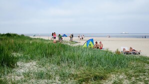 Une plage où l’on voit des gens se détendre, des tentes et un navire au loin.