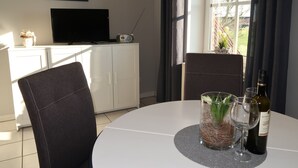Un coin repas avec une table ronde, des chaises, une bouteille de vin et un vase agrémenté de verdure.