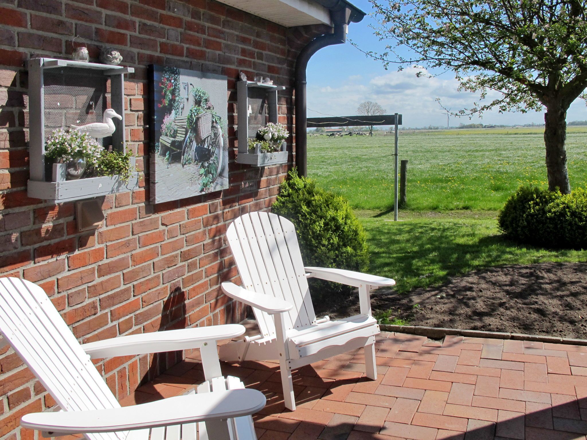 A brick building with two white Adirondack chairs outside, a brick patio, and a view of a green field.