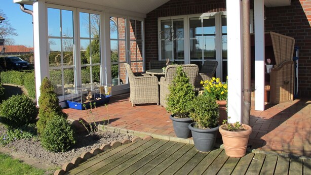 Une terrasse couverte, aménagée avec des meubles en osier, des plantes en pot et un mur en briques.