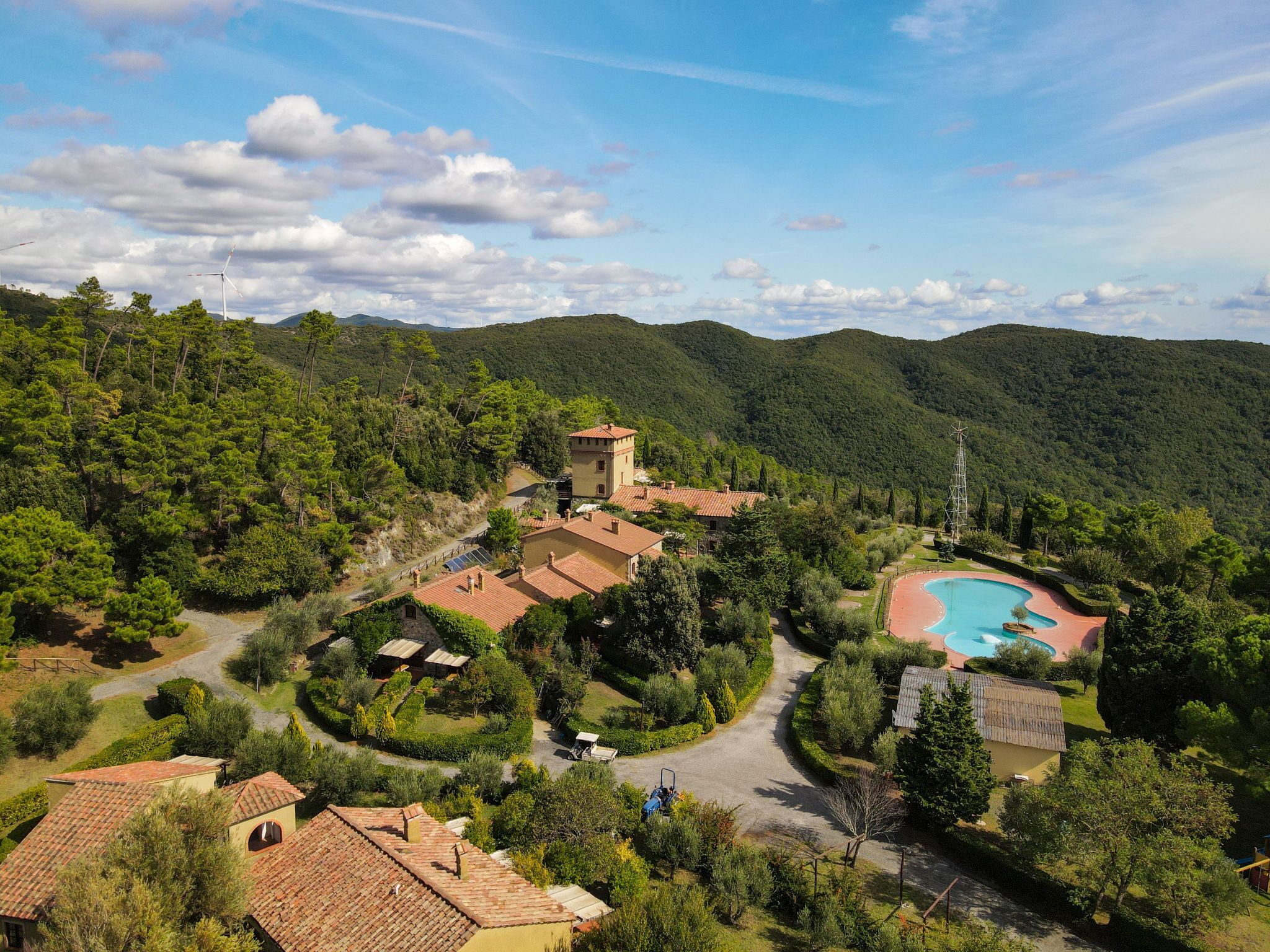 Et resort med swimmingpool, omgivet af frodig vegetation og bakker.