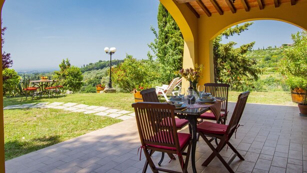Un patio al aire libre con una mesa dispuesta para comer, rodeado de sillas y vistas a un paisaje montañoso.