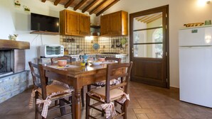 Una cocina rústica con armarios de madera, un protector de salpicadero de azulejos, una mesa de comedor con sillas, un televisor y un refrigerador.