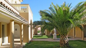 Un patio con palmeras, una estatua y un edificio con arcos y columnas.