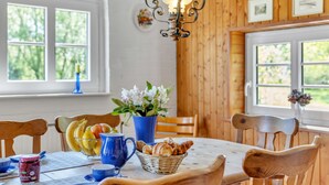 A dining area with wooden walls, a chandelier, and a table set with fruits, bread, and a vase of flowers.