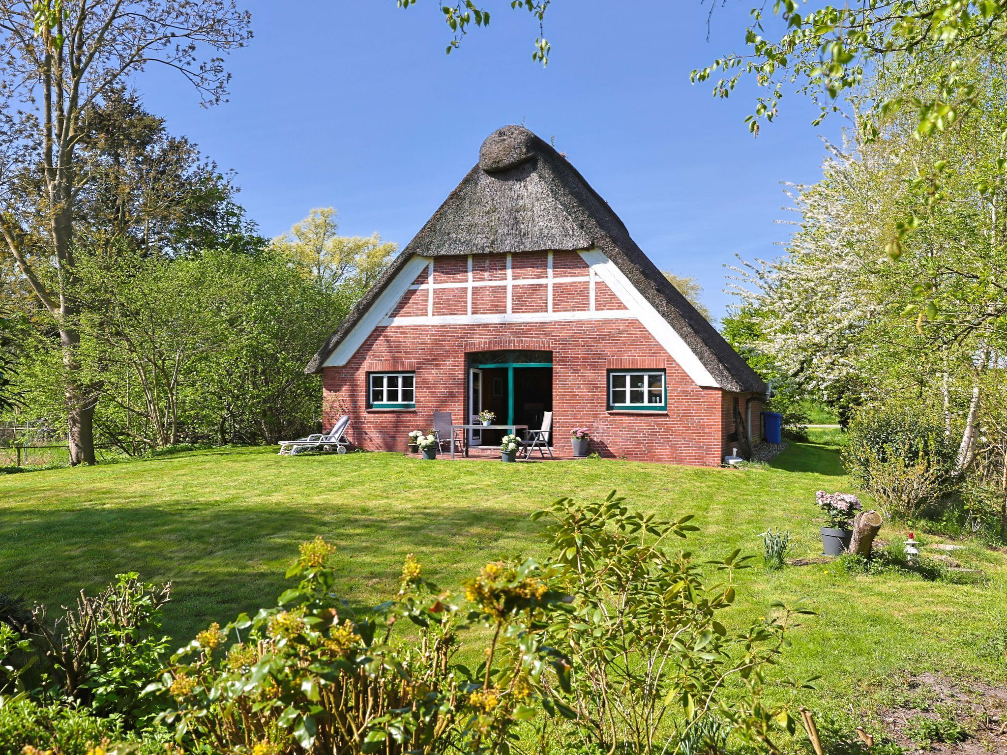 A traditional thatched-roof house with a brick exterior, surrounded by a well-maintained lawn and trees.