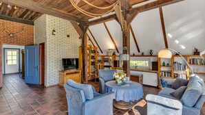 A spacious living area with a brick fireplace, wooden beams, and a large bookshelf.