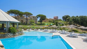 Piscina com espreguiçadeiras e guarda-sóis, cercada por edifícios e árvores.