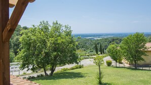 A view from a covered outdoor area with a wooden pergola, overlooking a lush green landscape with trees and a distant view of the sea. - Il Felciaione by Interhome (Riparbella)