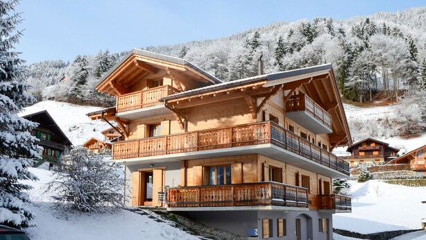 Un chalet en bois à plusieurs étages, doté de balcons, situé dans une région montagneuse enneigée.