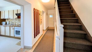 A hallway with a carpeted floor, a staircase with a handrail, and a kitchen area visible through an open door. - Wiegele by Interhome (Velden am Wörthersee)