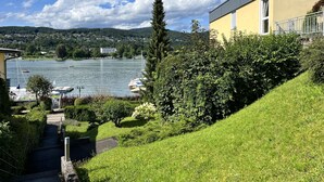 Une vue sur un lac avec des bateaux, un bâtiment jaune doté d’un balcon et une colline verdoyante.