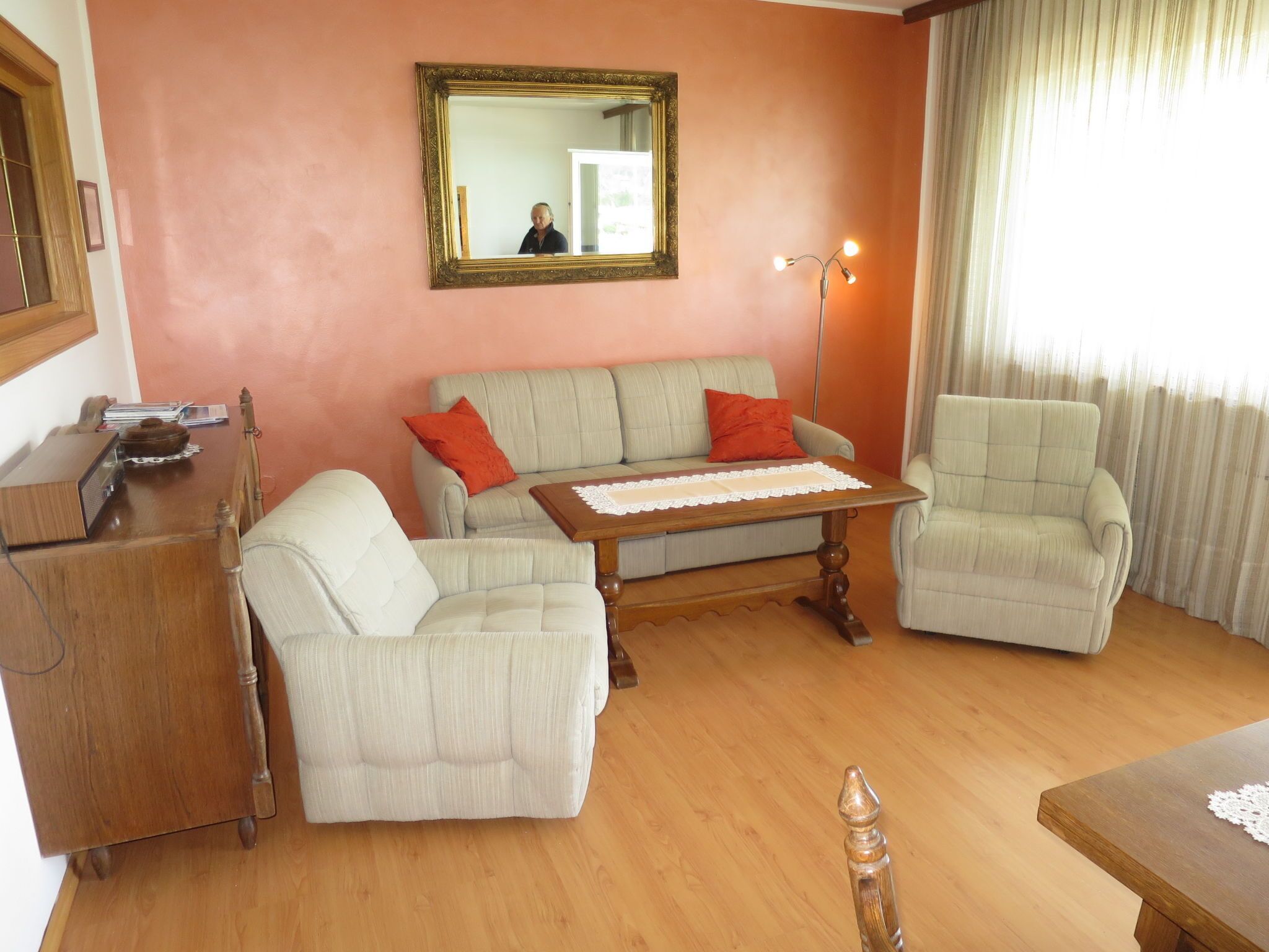 A living room with a sofa, two armchairs, a wooden coffee table, a lamp, and a mirror on the wall.