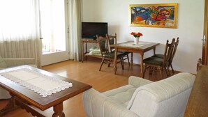 Un salon avec une table en bois, un canapé, une table à manger avec des chaises, un téléviseur et un tableau accroché au mur.