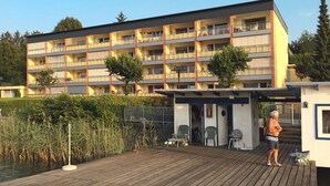 Un hôtel à plusieurs étages doté de balcons, d’un espace extérieur couvert avec des sièges et d’une terrasse en bois située au bord de l’eau.