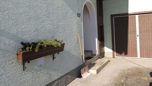 Un bâtiment doté d’un mur extérieur à la texture particulière, d’un banc en bois agrémenté de plantes, d’une enseigne portant le numéro « 127 » et d’une porte en bois.