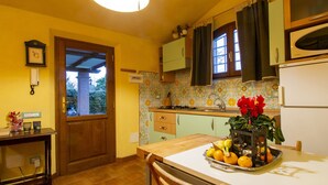A kitchen with a tiled backsplash, a wooden table with fruit, a refrigerator, and a window with curtains.