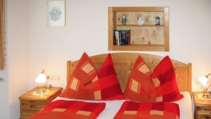 A neatly made bed with a red and beige checkered bedspread, two bedside lamps, and a wooden headboard. - Reinbacher by Interhome (Gröbming)