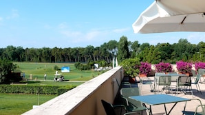 Een balkon met buitenmeubilair, een golfbaan op de achtergrond en een helderblauwe lucht.