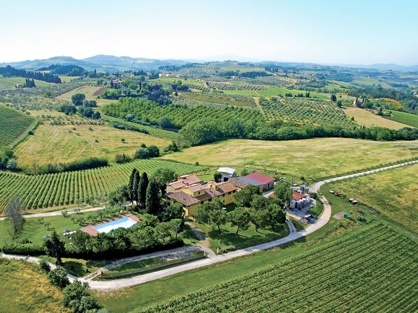 An aerial view of a vineyard with terraced fields, a central building with a red roof, and a swimming pool.